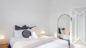 A neatly made bed with pillows and a blanket, a bedside lamp, and a mirror on the wall. - Brighton Vale, St. Kilda (St Kilda)