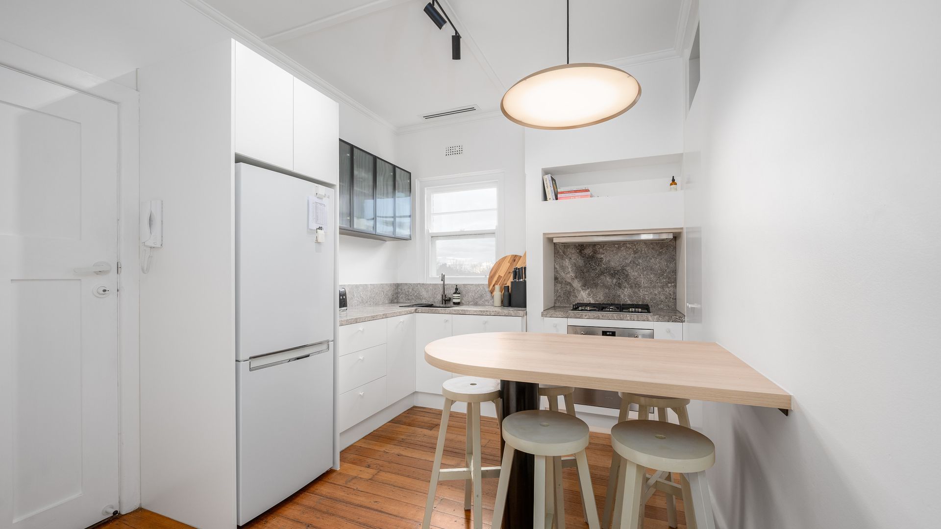 A compact kitchen with white cabinetry, a built-in oven, a sink, and a wooden dining table with stools.