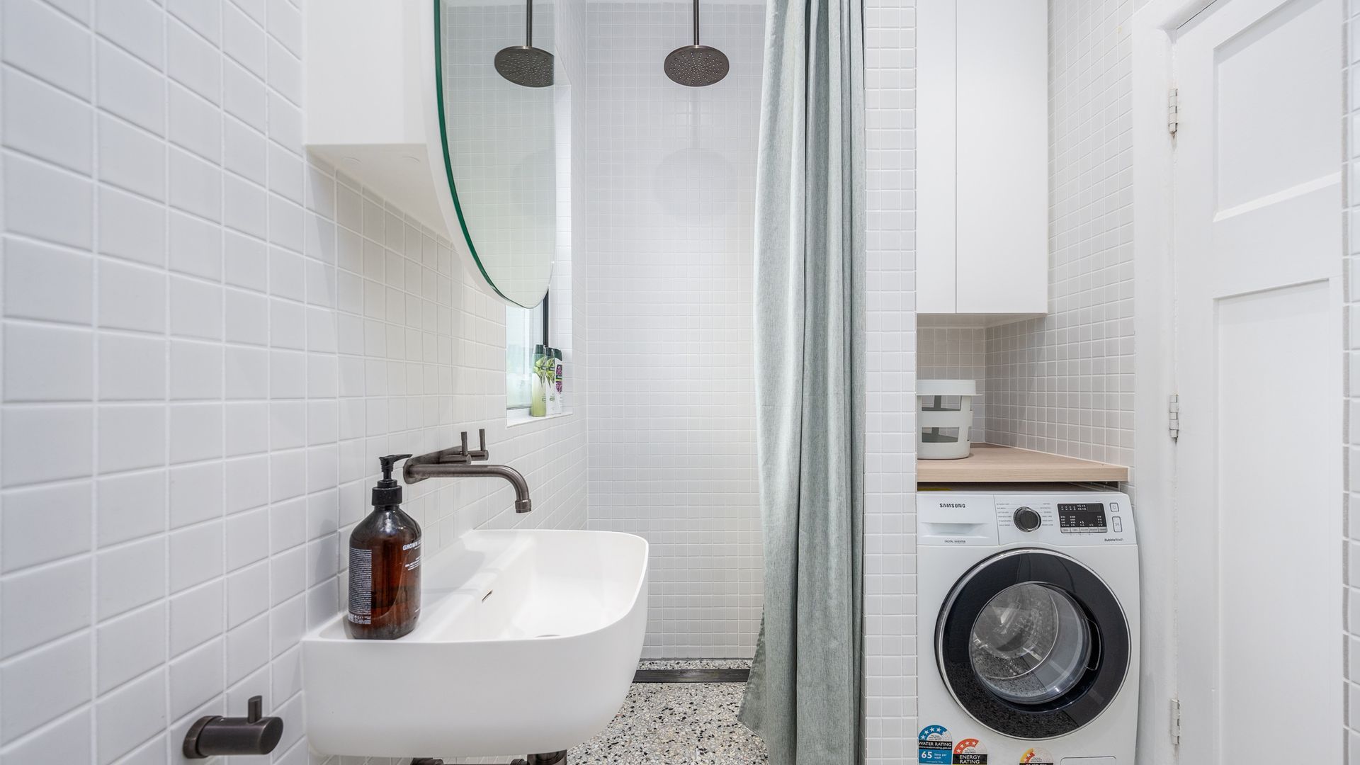 A modern bathroom with a white sink, a shower with a glass door, and a washing machine.