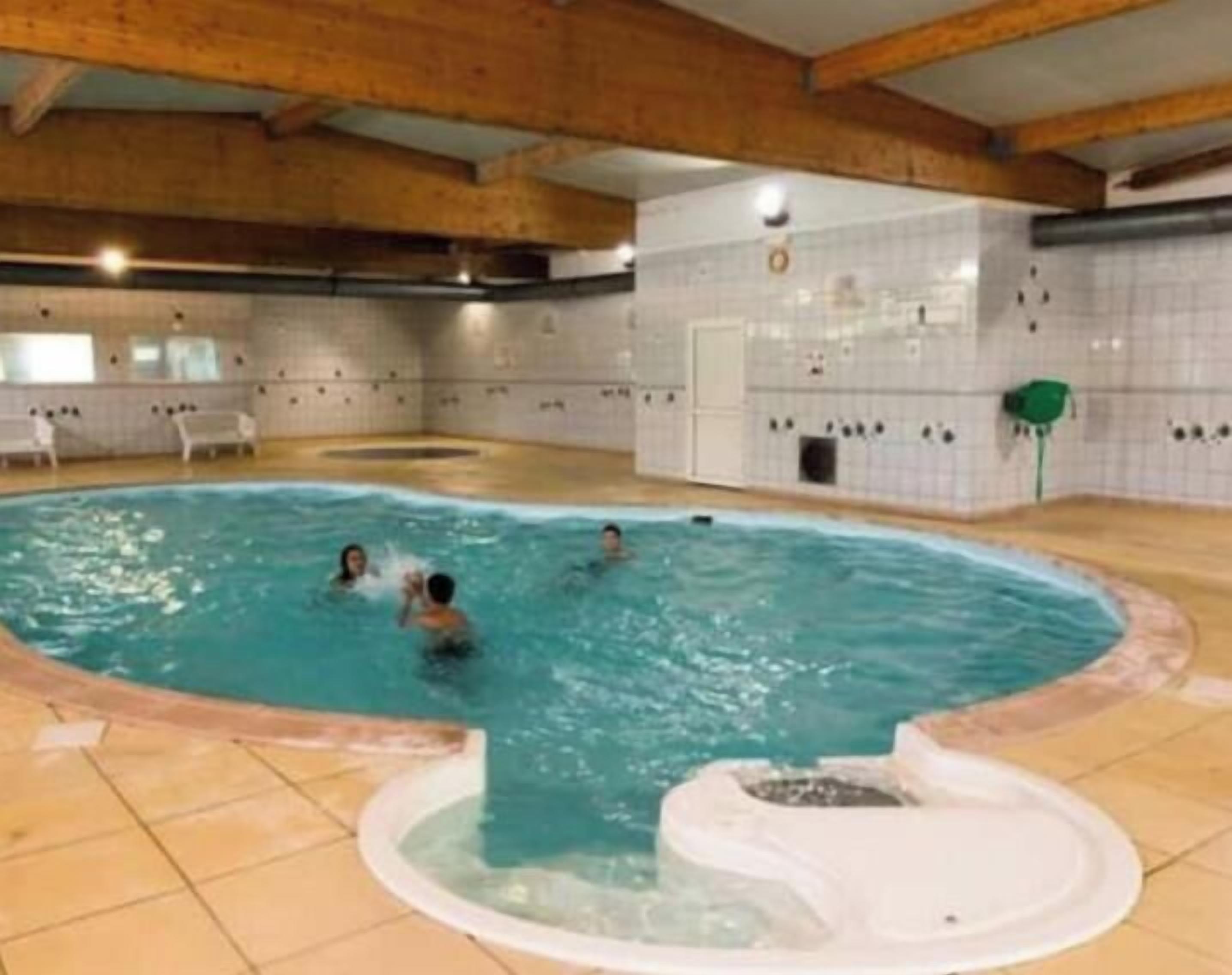 Ein Innenpool mit Fliesenboden, einer Whirlwanne und einer Holzbalkendecke.