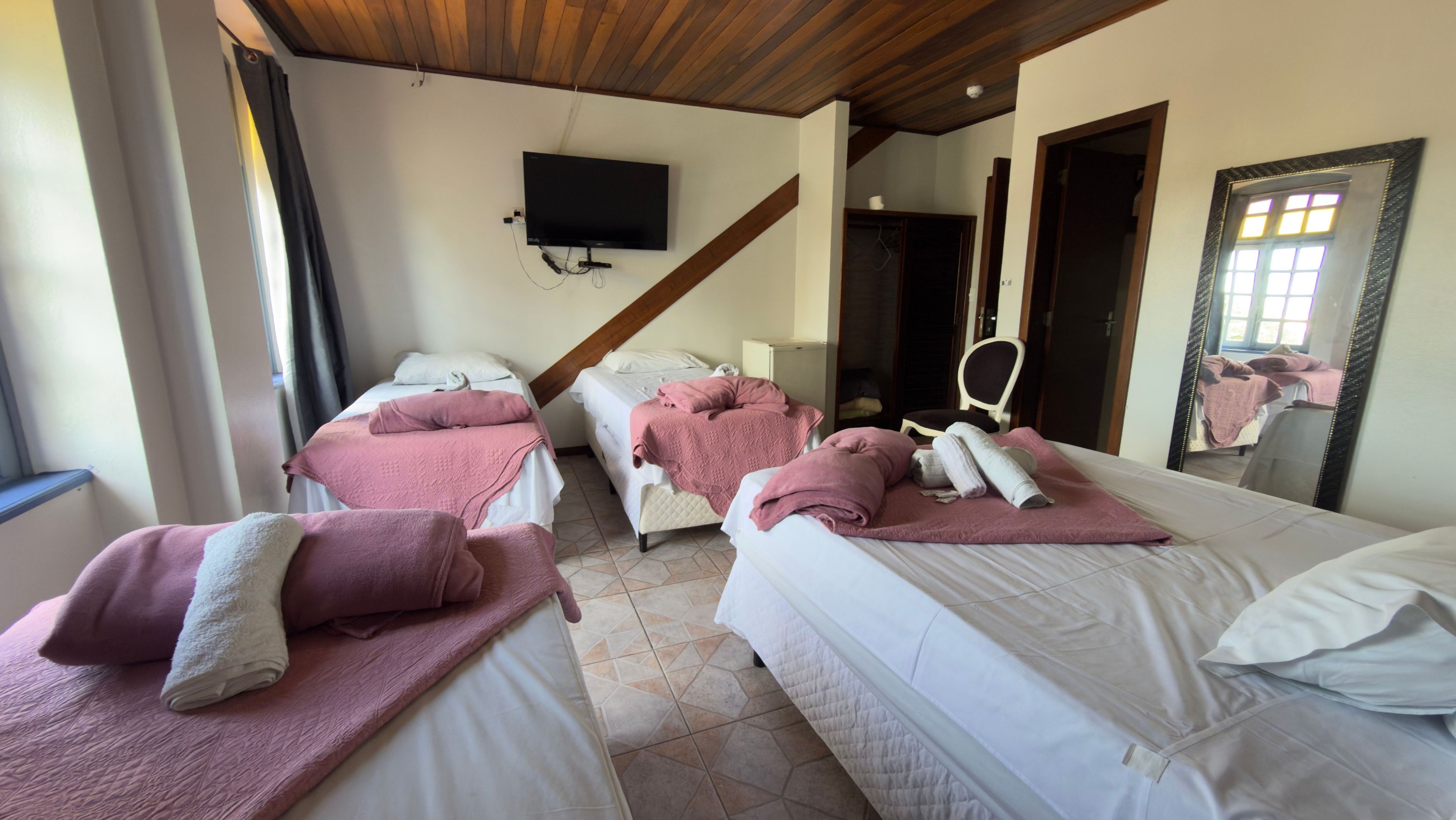 A hotel room with two beds, a television mounted on the wall, and a large mirror.