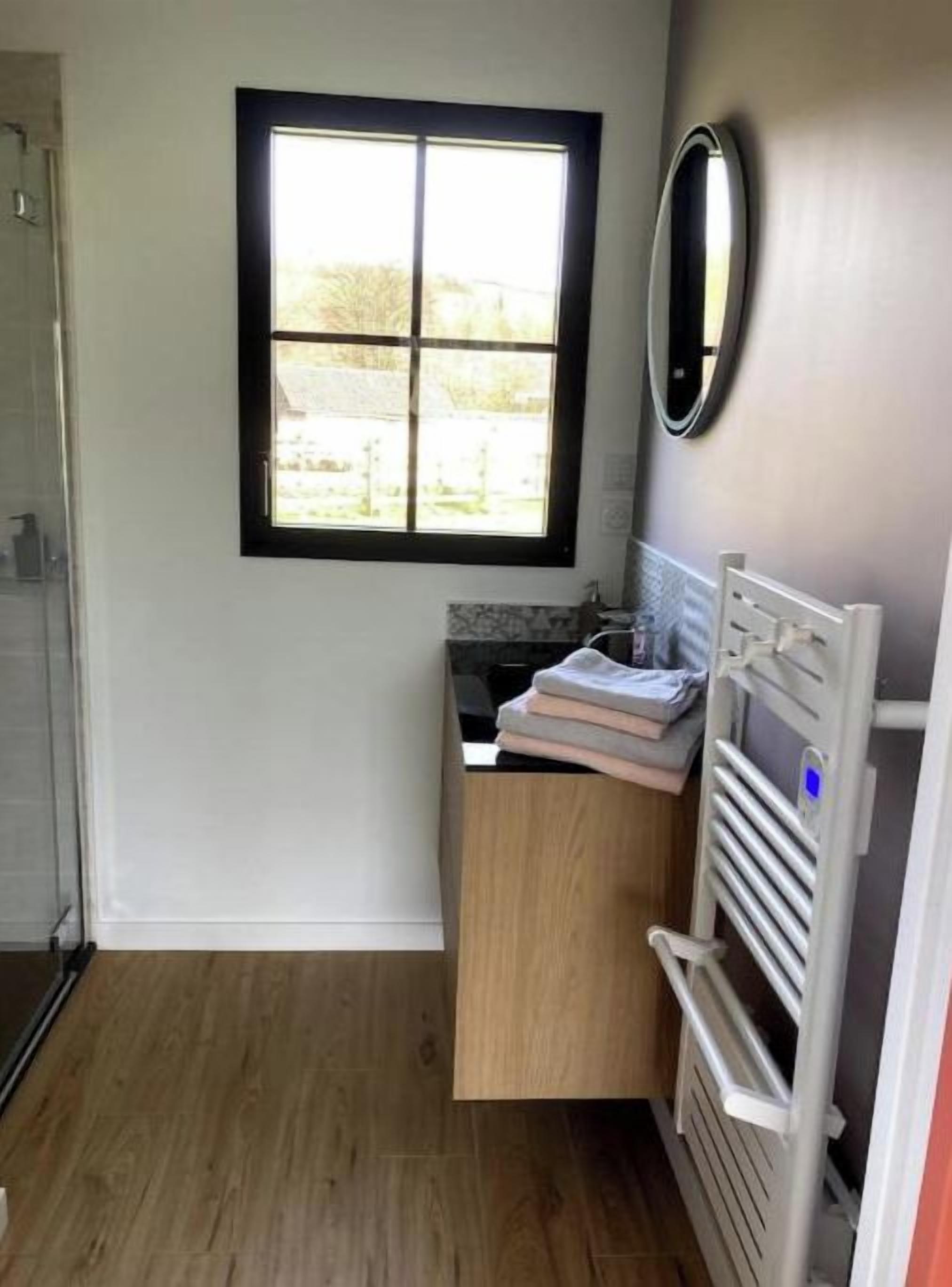 Ein kleines Badezimmer mit Fenster, Spiegel und Handtuchhalter.