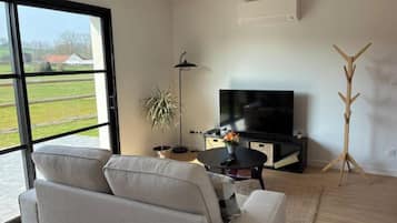 Una sala de estar moderna con un sofá, un televisor, una lámpara de pie y un atril.
