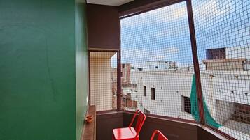 A balcony with a view of the cityscape, a red chair, a wooden shelf, and a hanging light fixture.