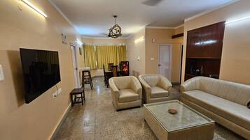 A living room with a flat-screen TV, two armchairs, a sofa, a coffee table, and a ceiling fan.