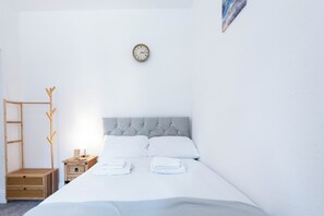 Una camera da letto con un letto, un comodino in legno, una sveglia a muro e un appendiabiti.
