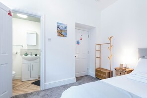 A room with a bed, a wooden coat rack, a bathroom with a sink and cabinets, and a door with a 'Fire action' sign. - The Stanley Arms Hotel by Guestz (Seascale)