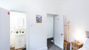 Quarto de hotel com banheiro, cama, mesa de cabeceira e porta-roupas.