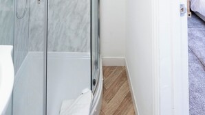 Casa de banho moderna com chuveiro envidraçado, lavatório branco e chão de madeira.