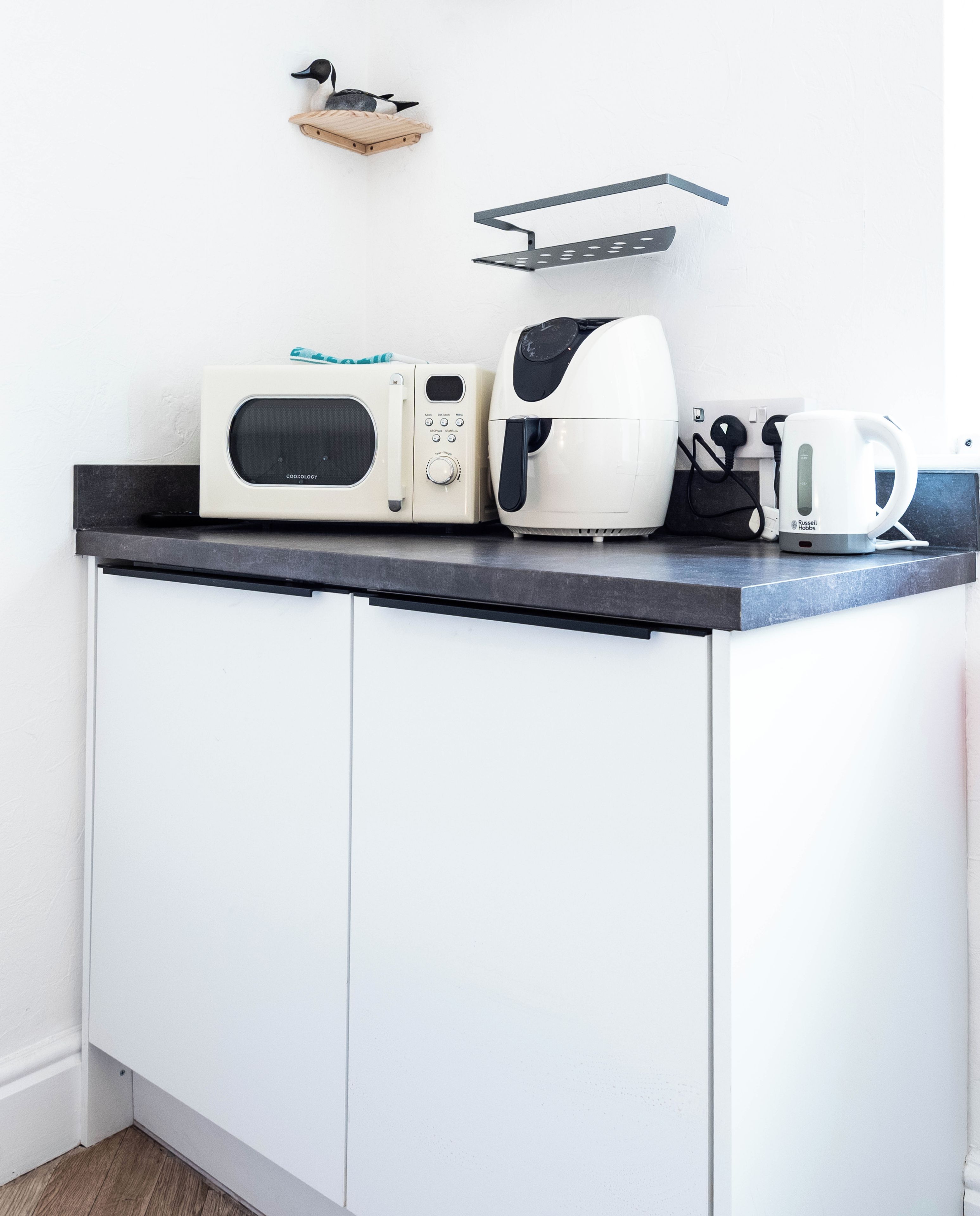 A kitchenette with a microwave, coffee maker, and kettle on a countertop.