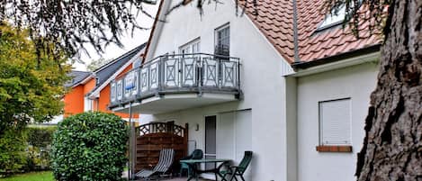 A residential building with a balcony, a patio with outdoor furniture, and a well-maintained lawn.