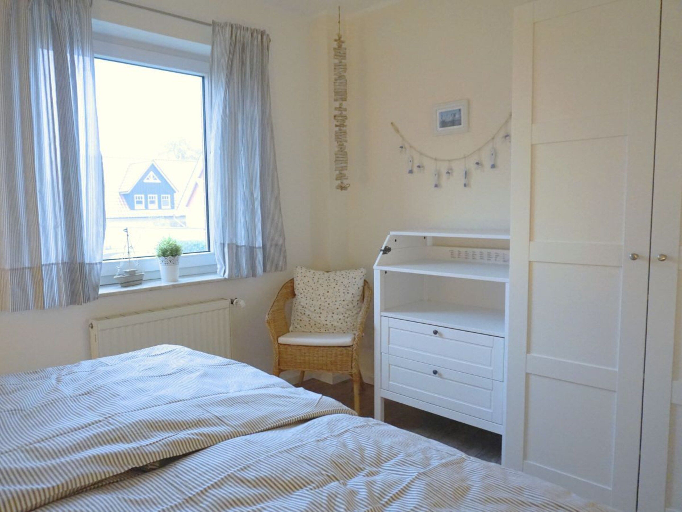 A bedroom with a bed, a chair, a dresser, and a window with curtains.