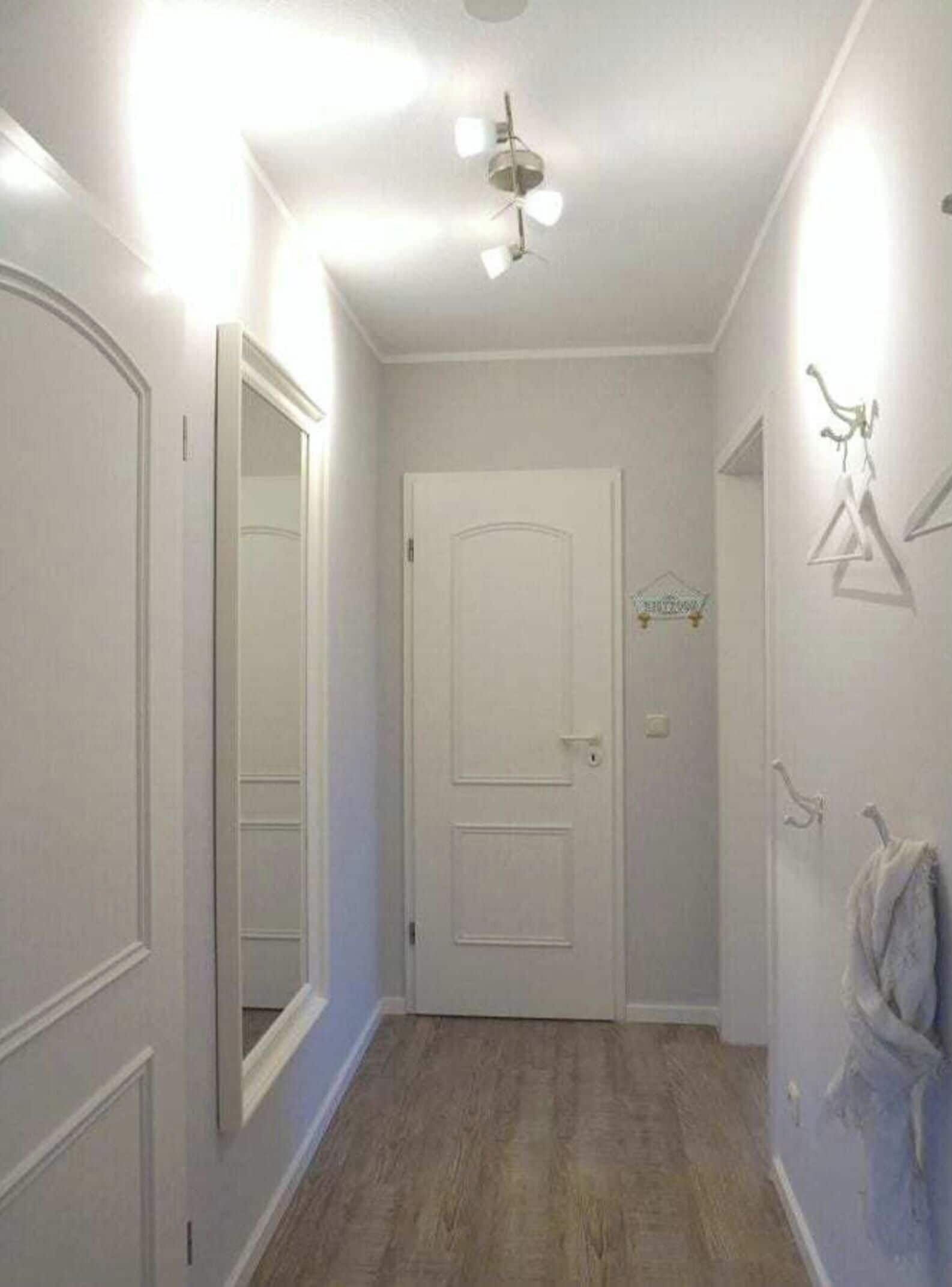 A narrow hallway with a white door, a ceiling fan, and a coat rack with a towel.