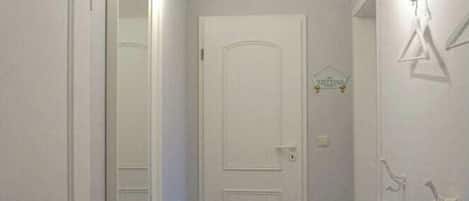 Un pasillo estrecho con una puerta blanca, un ventilador de techo y un perchero con una toalla.