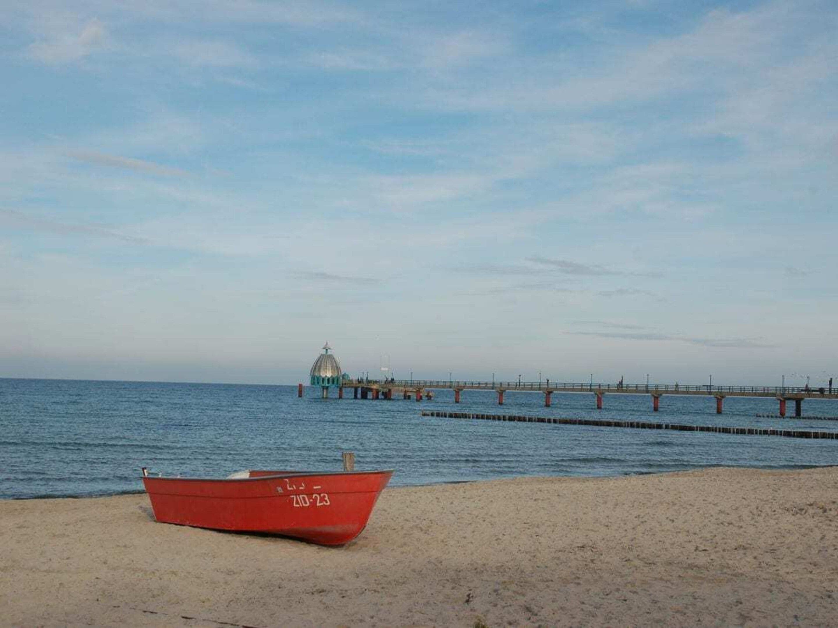 Una playa con un bote rojo y un muelle que se adentra en el agua.