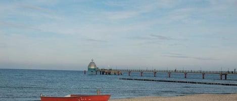 Una playa con un bote rojo y un muelle que se adentra en el agua.