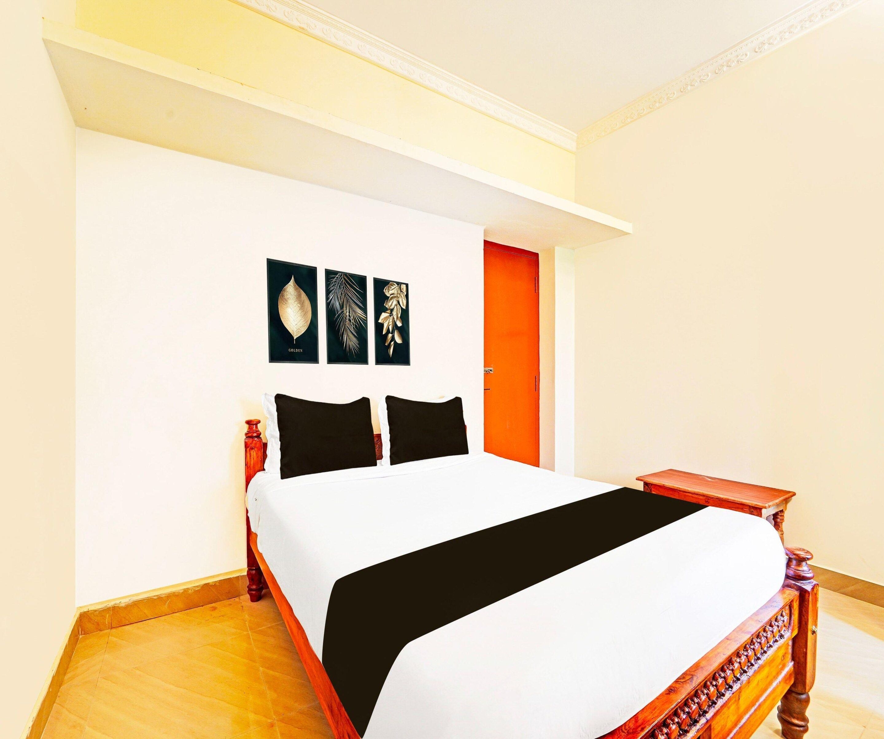 Una habitació d'hotel amb un llit, una taula de nit, una banca de fusta i una porta.