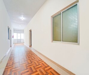 A hallway with a wooden parquet floor, white walls, and a large window with a textured glass pane. - Deluxe KS Comfort (Chidambaram)
