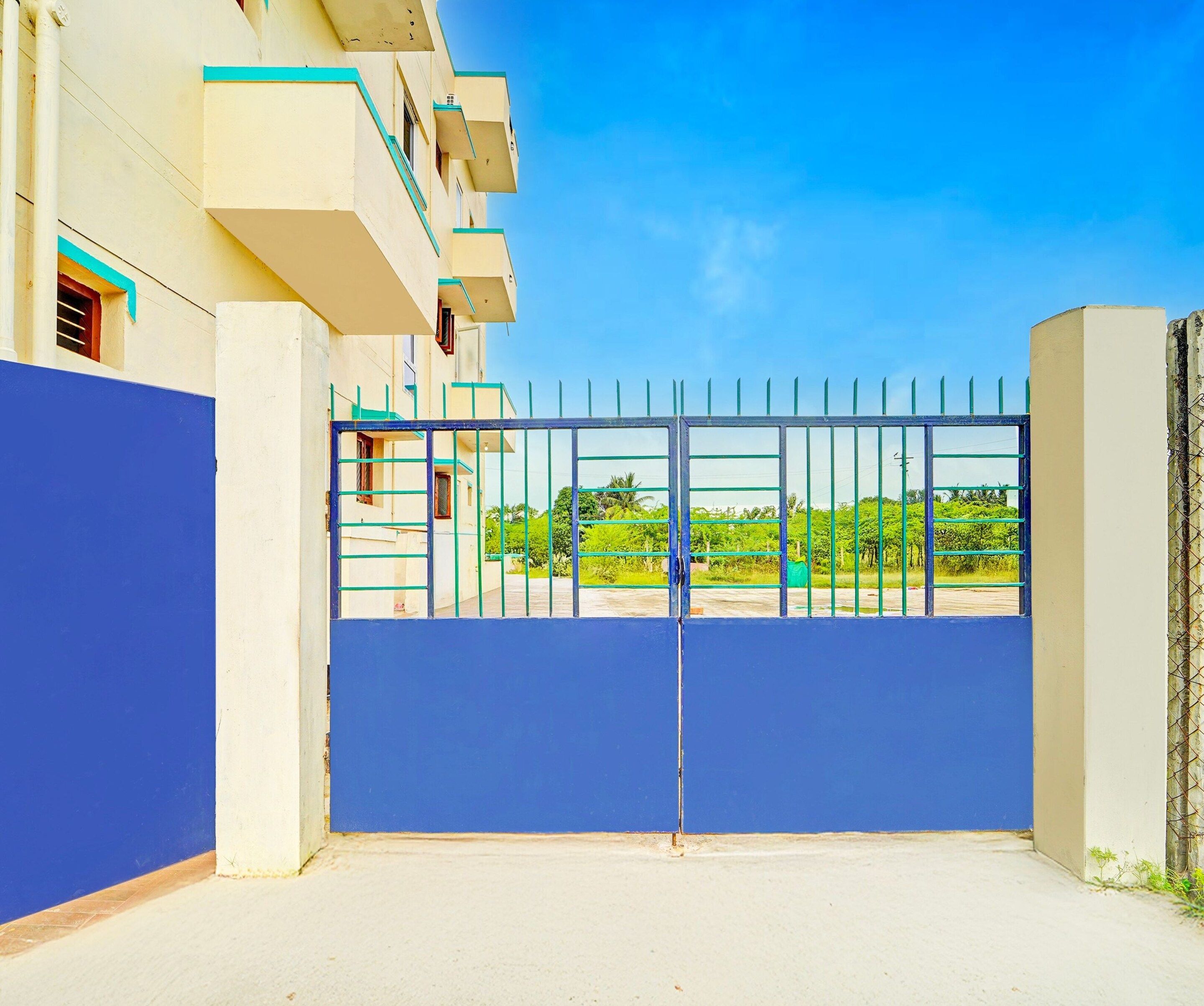 A gated entrance to a building with a blue fence and a clear sky.