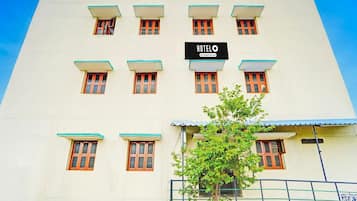 Un edificio de hotel con un cartel que dice 'HOTEL' y un logotipo de la empresa. Se ven varias ventanas con marcos de madera y un árbol en primer plano.