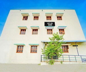 A hotel building with a sign that reads 'HOTEL' and a company-serviced logo. There are multiple windows with wooden frames and a tree in front. - Deluxe KS Comfort (Chidambaram)