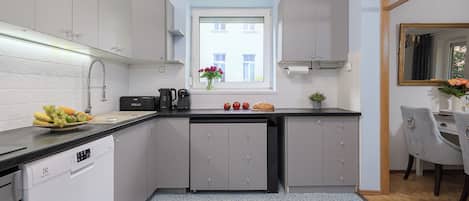 A modern kitchen with grey cabinets, a black countertop, a built-in dishwasher, and a window with a view of buildings.