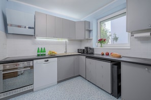 A modern kitchen with grey cabinets, a black countertop, and a window with a view of trees. - Lumina 3-room Apt w/ Balcony I Center (Warszawa)