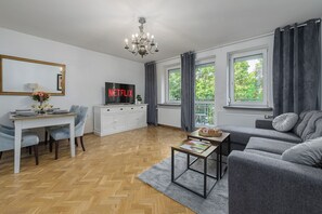 A modern living room with a television, sofa, dining table, and a chandelier. - Lumina 3-room Apt w/ Balcony I Center (Warszawa)