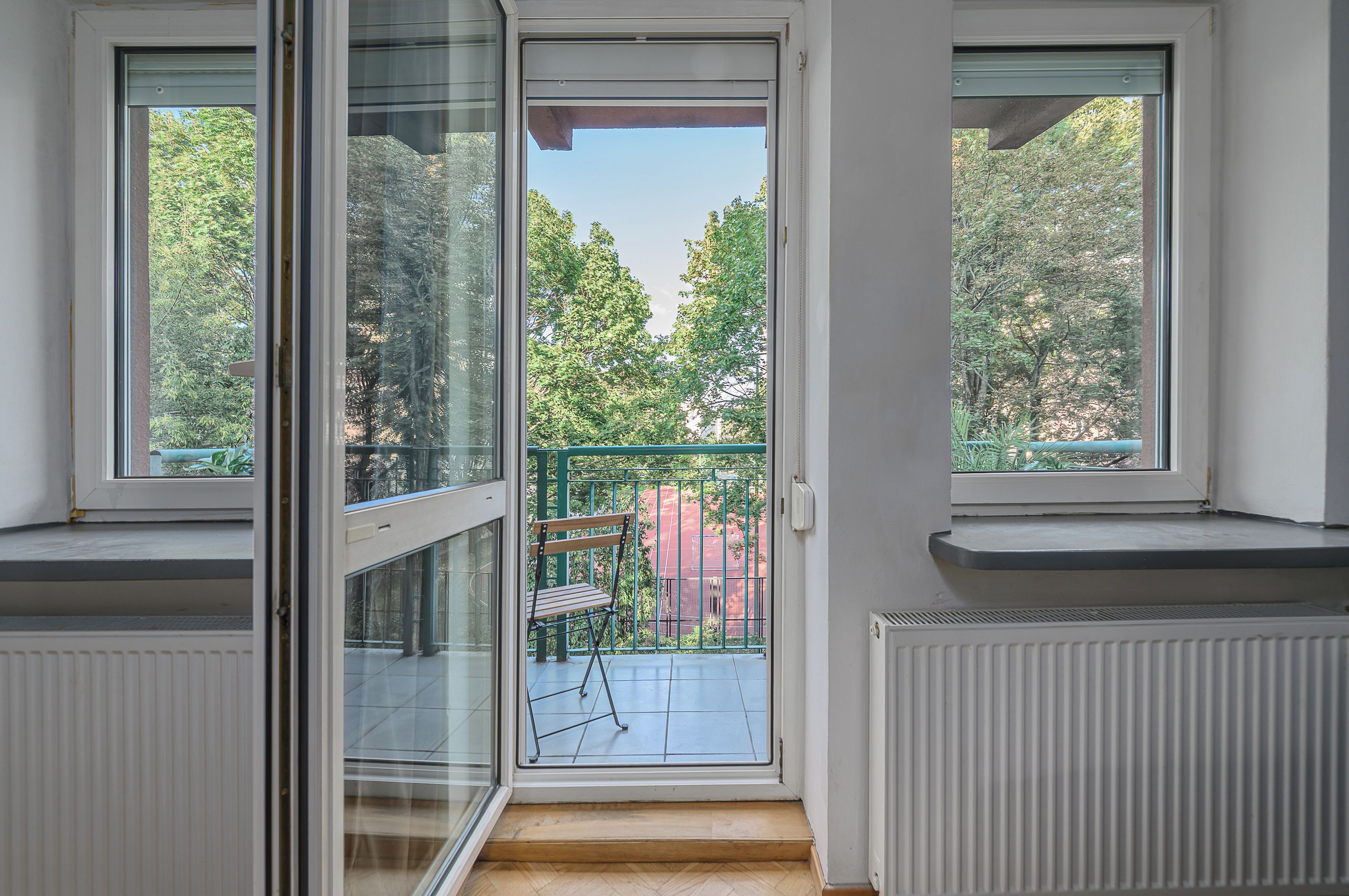 Ein Zimmer mit einer Schiebetür zu einem Balkon, auf dem ein Stuhl und ein grüner Zaun stehen.