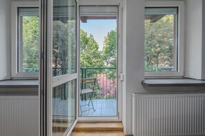 A room with a sliding glass door leading to a balcony with a chair and a green fence. - Lumina 3-room Apt w/ Balcony I Center (Warszawa)