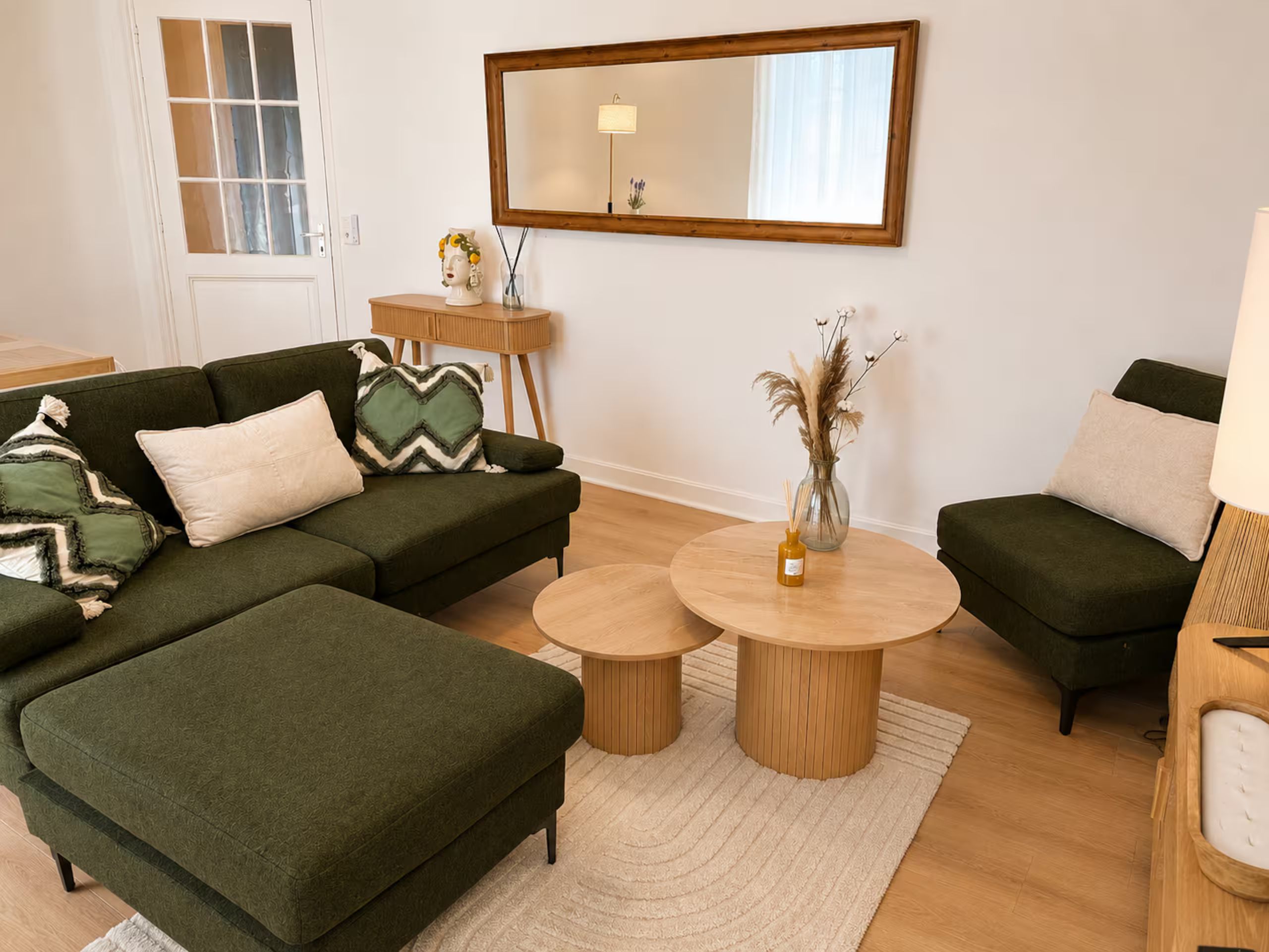 Un salon avec deux canapés verts, une table basse ronde et une table d’appoint sur laquelle se trouve un vase.