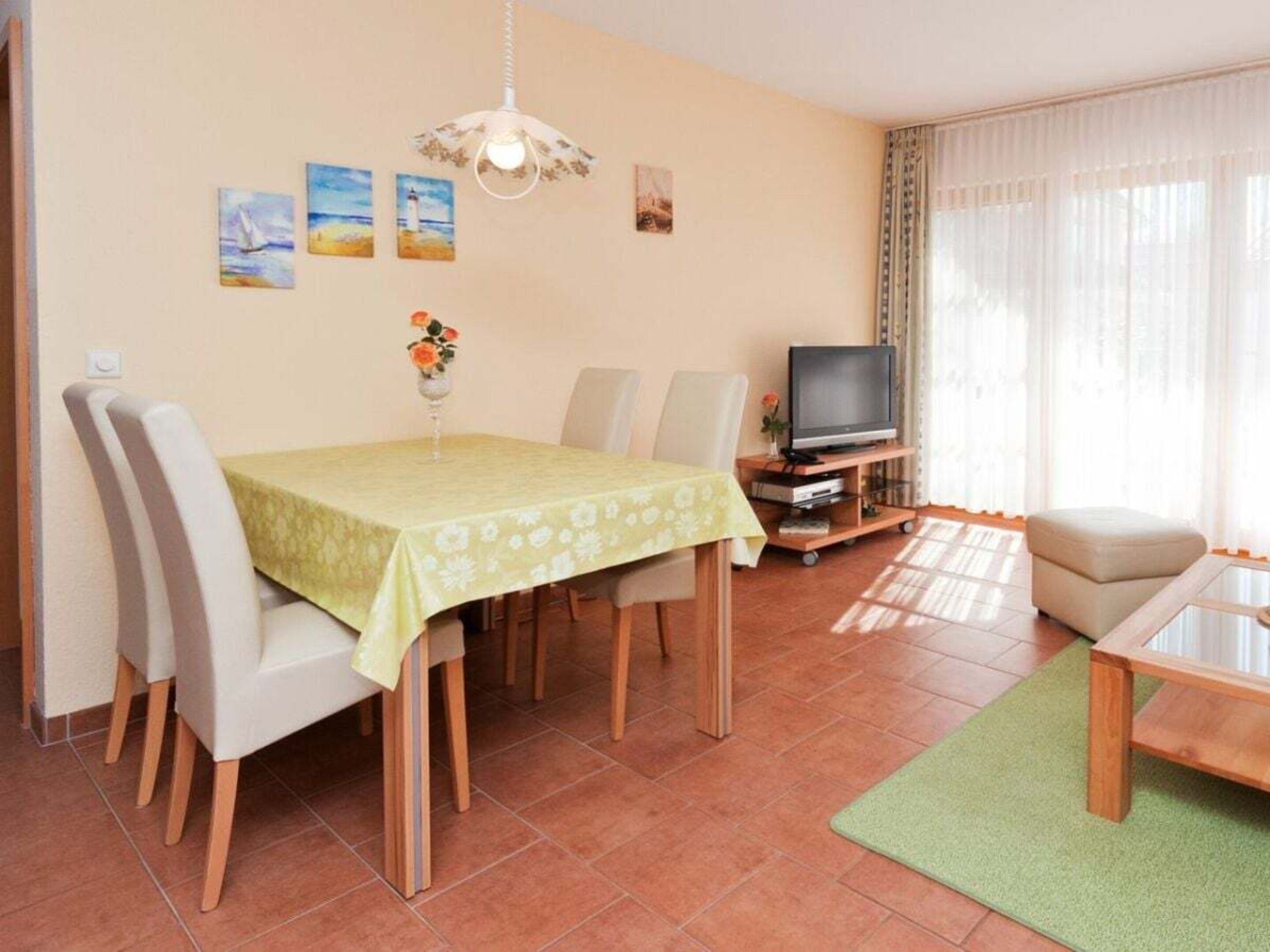 Un salon comprenant une table à manger, des chaises, un téléviseur posé sur un meuble et des œuvres d’art accrochées au mur.