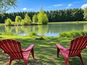 Two red Adirondack chairs facing a calm lake with a forested backdrop.