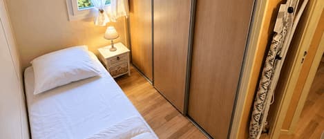 Een slaapkamer met een bed, nachtkastje met een lamp, een kledingkast en een raam met gordijnen.
