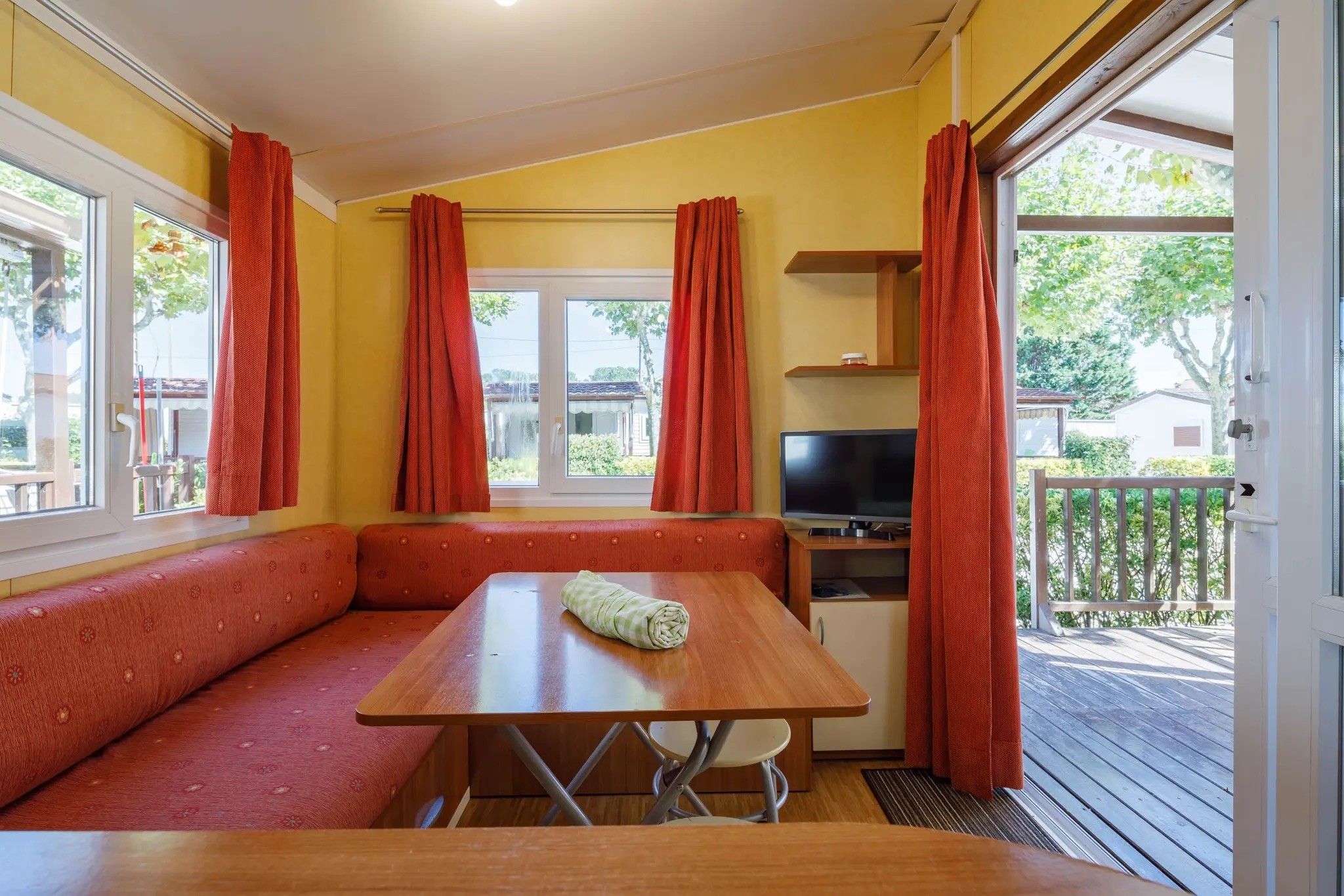 Una habitación con una mesa de madera, un banco, un televisor y una ventana con cortinas.