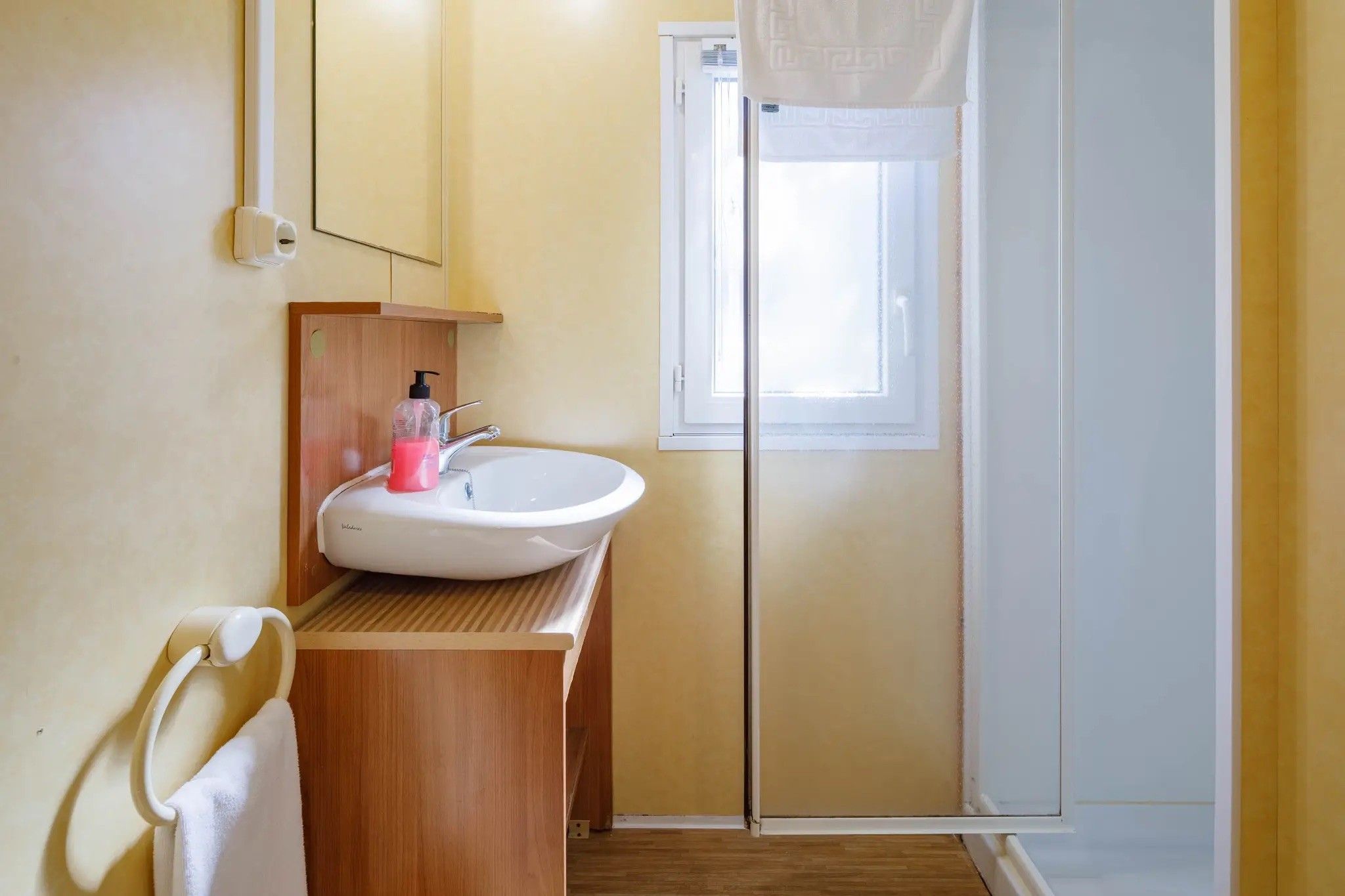 Un baño con tocador de madera, lavabo blanco y cabina de ducha de vidrio.