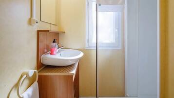 Un baño con tocador de madera, lavabo blanco y cabina de ducha de vidrio.