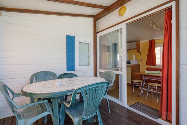 Un espacio de comedor al aire libre techado, con una mesa y sillas, un ventanal corredizo que da a una cocina y una terraza de madera.