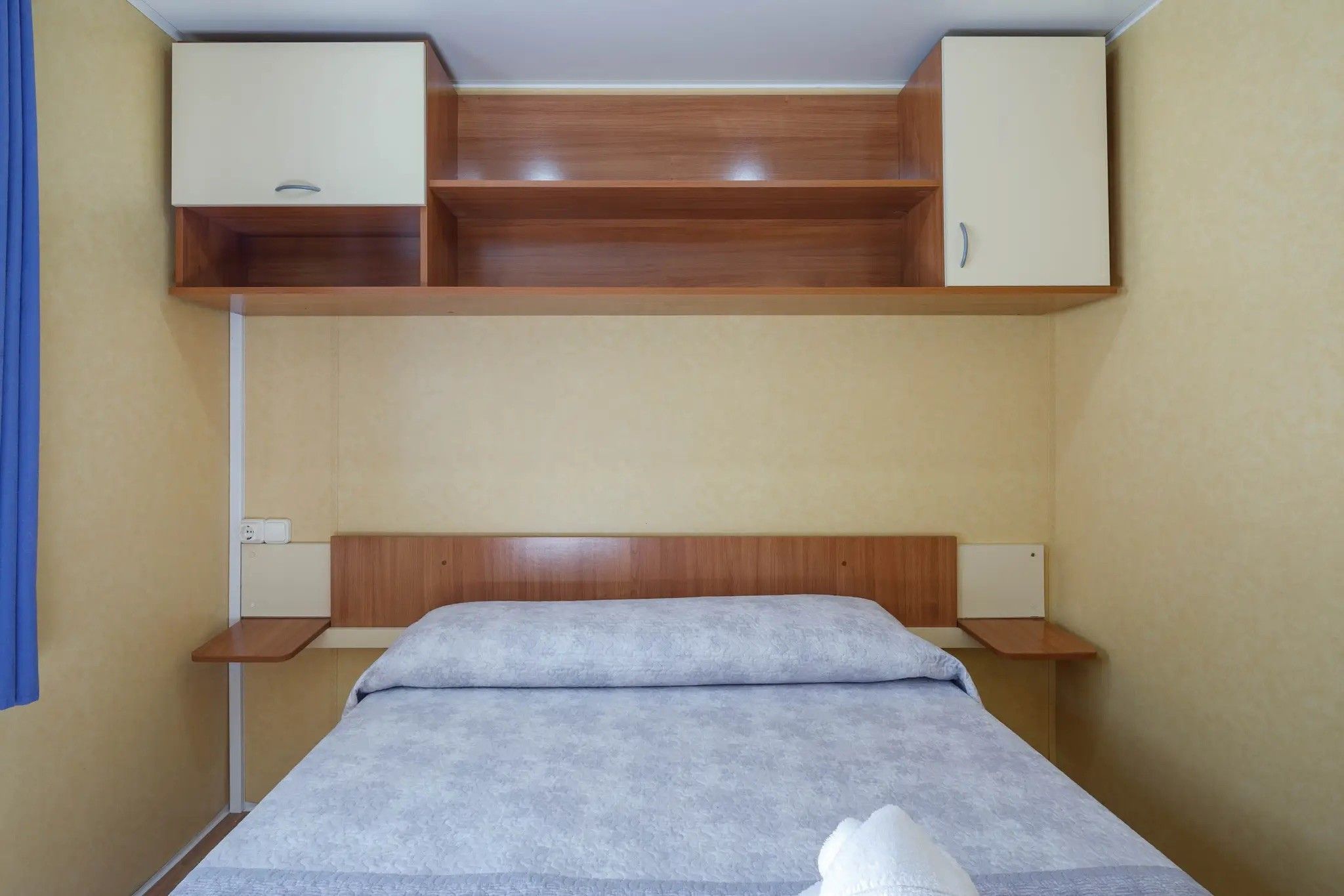 Un lit simple avec une tête de lit en bois, une table de chevet et une étagère intégrée au-dessus du lit.