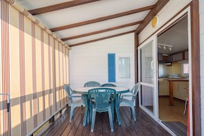 Un espacio exterior cubierto con una mesa y sillas, un divisor corredizo que da a una cocina, y una pared a rayas.