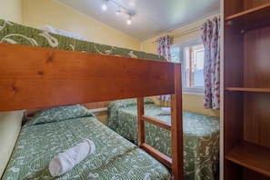 Habitación con literas, cabecera de madera, dos camas con ropa de cama estampada, una ventana con cortinas y un estante de madera.