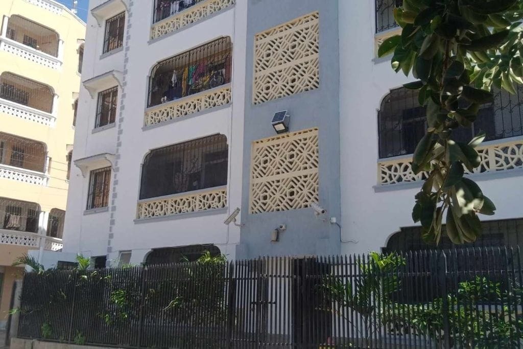 Un immeuble à plusieurs étages doté de balcons, d’une clôture en métal noir et d’un arbre au premier plan.