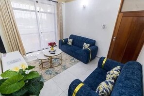 A living room with a blue sofa set, a small round coffee table, and a potted plant. - Serene 1-bedroom apartment in the heart of Mombasa (Mombasa)