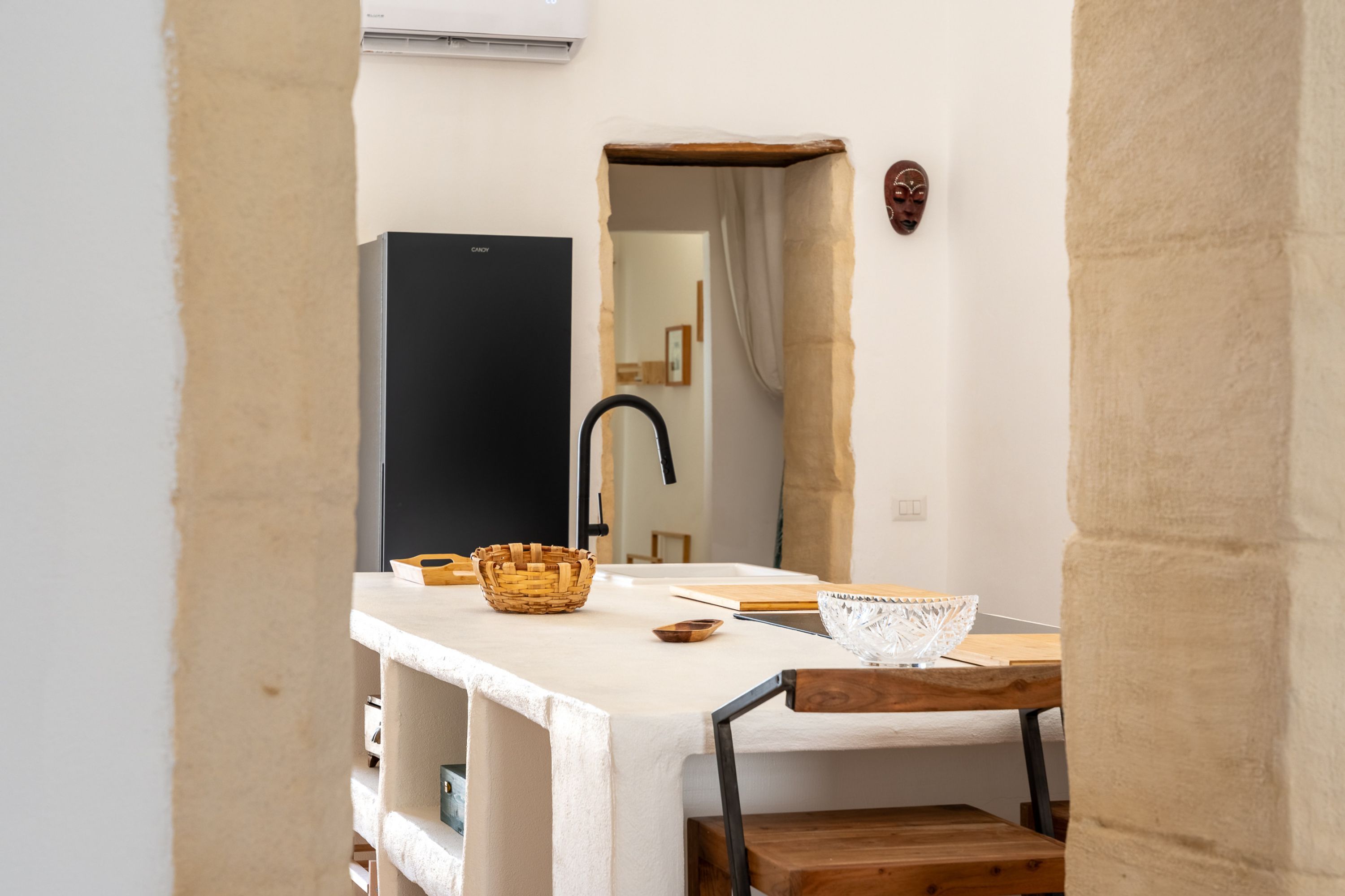 A small, narrow room with a white sink, a wooden chair, a woven basket, and a wooden table.