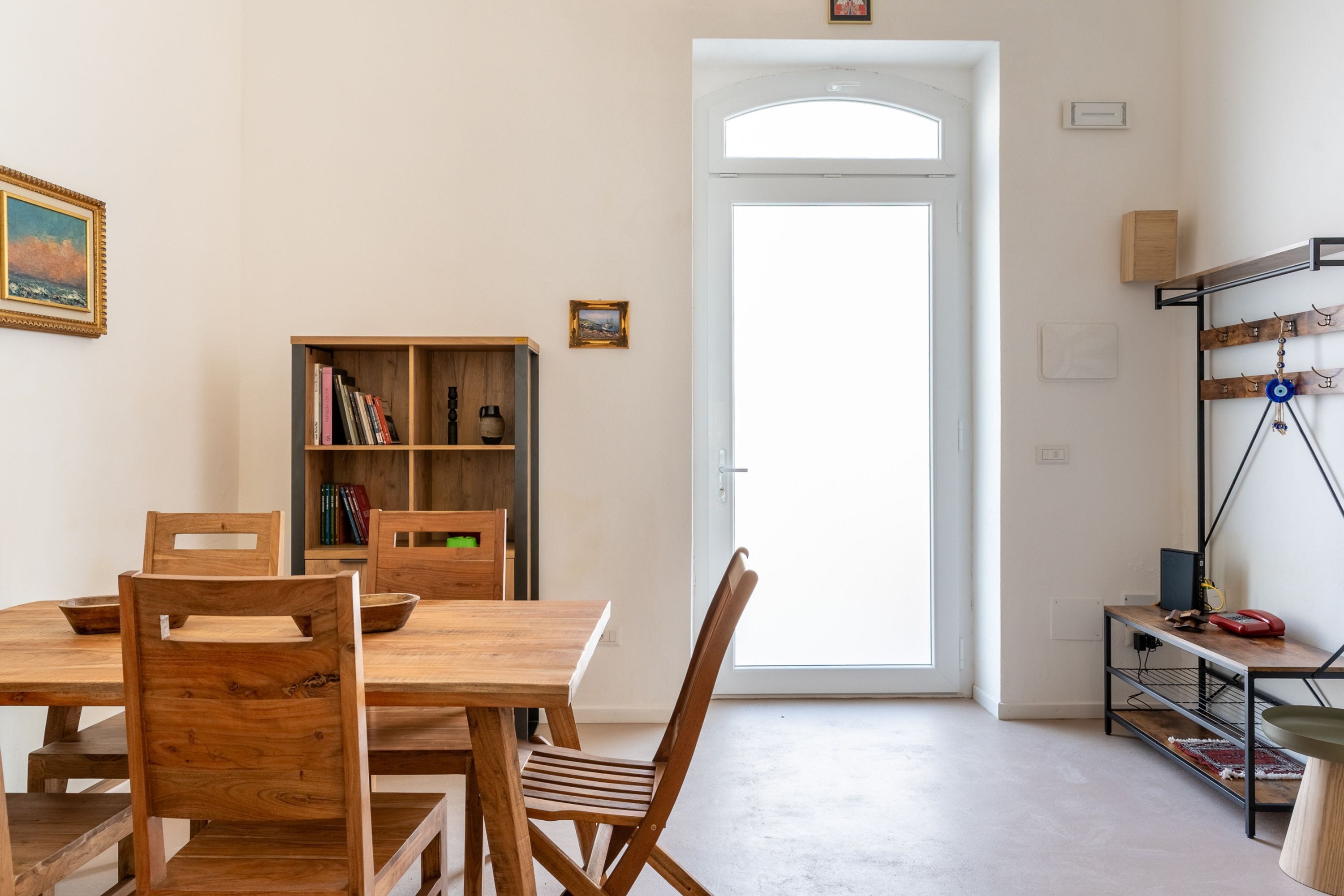 Un comedor con una mesa y sillas de madera, una estantería y una puerta que da al exterior.