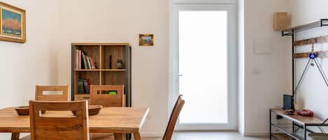 A dining area with a wooden table and chairs, a bookshelf, and a door leading outside.