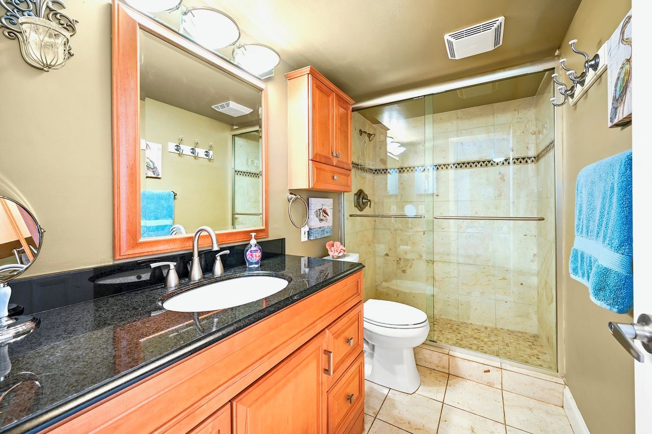 Ein Badezimmer mit Waschbecken, Spiegel, Schrank, Toilette und einer Duschkabine aus Glas.