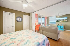 Ein Schlafzimmer mit Bett, Sofa, Wanduhr, Fenster mit Aussicht und Deckenventilator.
