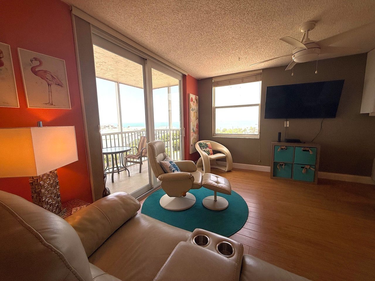 A living room with a sofa, two armchairs, a coffee table, a TV, and a balcony with a view.
