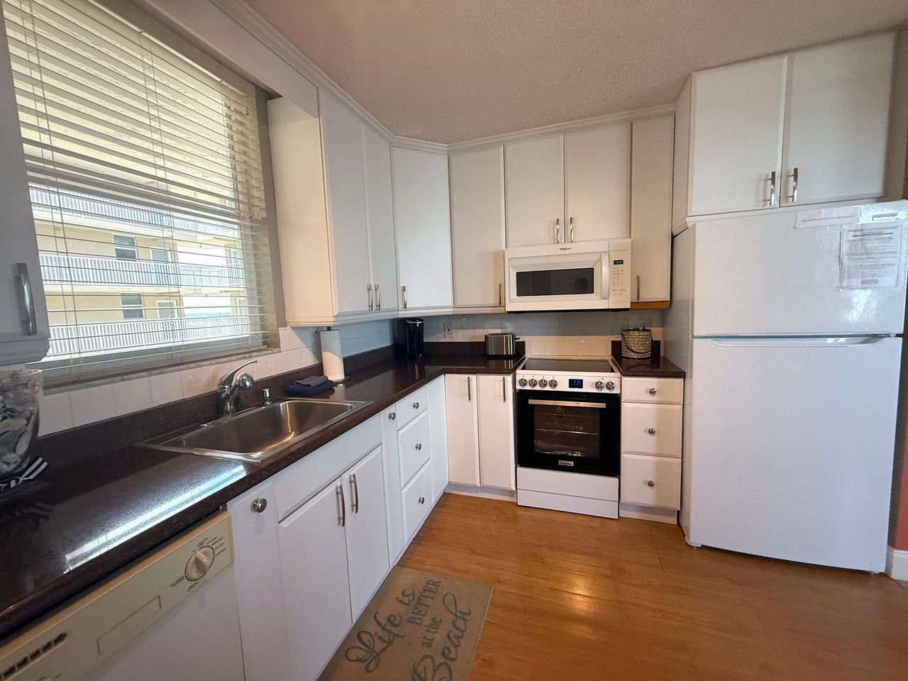 A compact kitchen with white cabinets, a stainless steel sink, a microwave, an oven, and a white refrigerator.